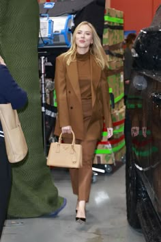 a woman is walking down the street carrying a handbag and wearing a brown suit