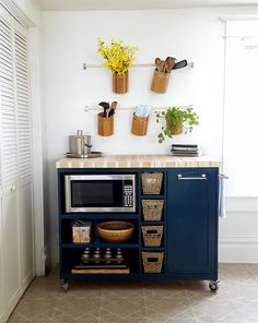 a kitchen area with a microwave, potted plants and baskets on the wall