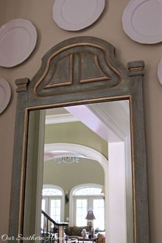 a mirror that is hanging on the wall in front of a table with plates above it