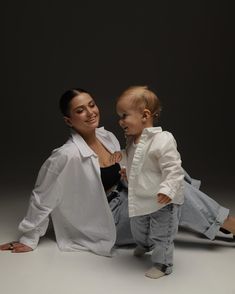 a woman sitting next to a baby on the ground