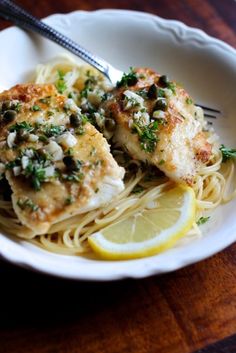 a white bowl filled with pasta and chicken on top of a wooden table next to a fork