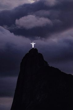 a person standing on top of a mountain with a cross in the sky above them