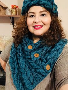 a woman wearing a blue knitted hat and scarf with buttons on the front, smiling at the camera