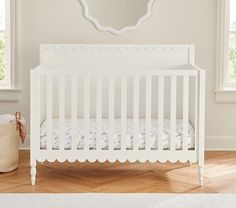 a white baby crib in a room with wooden flooring and large round mirror on the wall