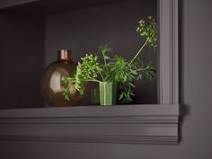 a green vase filled with plants on top of a shelf next to a gold vase