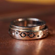 two silver rings with harry potter's glasses engraved on the sides, sitting on a wooden surface