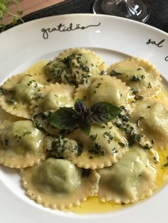 a white plate topped with ravioli covered in cheese and spinach next to a glass of wine