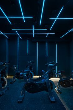 there are many exercise bikes in the room with neon lights on the wall behind them