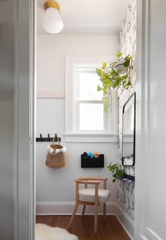 a white room with a chair, mirror and plant on the window sill in it