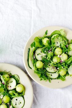 two white plates filled with green vegetables on top of a table cloth next to each other