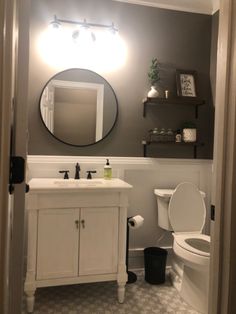 a white toilet sitting next to a bathroom sink under a mirror on top of a wall