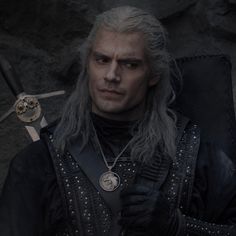 a man with grey hair holding two swords in his hand and wearing black leather clothes