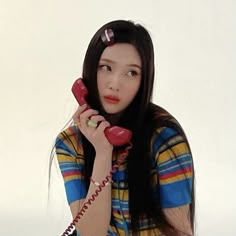 a woman sitting on the floor while talking on a red phone with her hand up to her ear