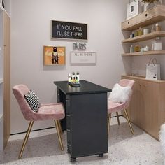 two pink chairs sit in front of a black desk and shelving with pictures on the wall