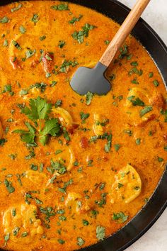 a skillet filled with red curry and chicken in a creamy broth, garnished with cilantro