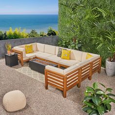 an outdoor living area with wooden furniture and plants on the patio overlooking the ocean in front of it