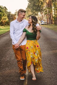 a man and woman are walking down the road holding each other's hands as they look at each other