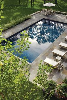 an outdoor swimming pool with lounge chairs and umbrellas next to it in the grass