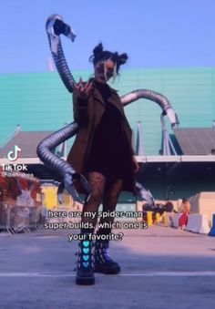 a woman in black dress and boots standing on top of a skateboard with her arms stretched out