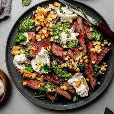 grilled flank steak with pesto and burrata sauce on a black plate