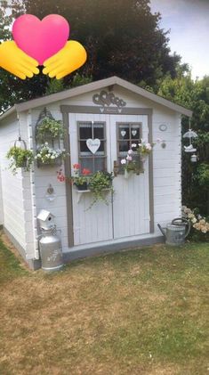 a small white shed with flowers in the window and a heart shaped balloon above it