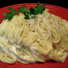 a red plate topped with pasta covered in sauce and garnished with parsley