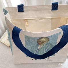 a white bag with a blue handle and a painting on the front, sitting on top of a table