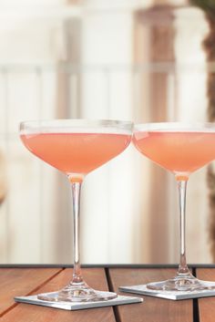 two glasses filled with pink liquid sitting on top of a wooden table next to each other