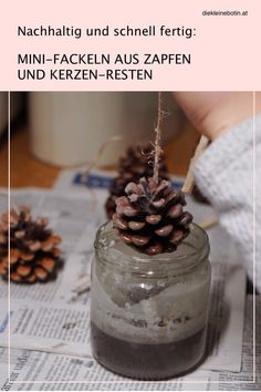 a person holding a small pine cone on top of a jar filled with dirt and sand