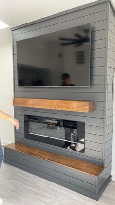 a man standing in front of a flat screen tv mounted on a wall next to a fireplace