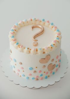 a white cake with blue, pink and gold sprinkles has a question mark on it