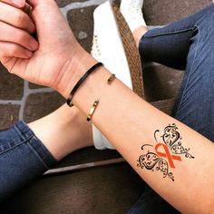 a woman's arm with a tattoo on it that has an orange ribbon in the shape of a heart