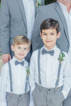 two young boys wearing grey suspenders and bow ties, standing next to each other