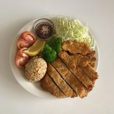 a white plate topped with meat and veggies next to a dipping sauce on top of it