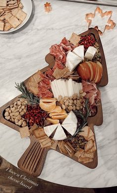 a wooden platter filled with cheese, meats and crackers on a marble table