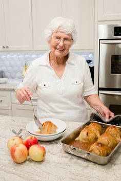 an older woman is preparing food in the kitchen with apples on the counter next to her