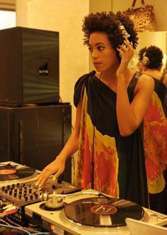 a woman in a black dress is using a dj's turntable and headphones