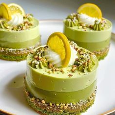 three desserts on a white plate topped with green and yellow frosting, garnished with nuts