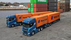 two blue and orange semi trucks parked next to each other in front of shipping containers