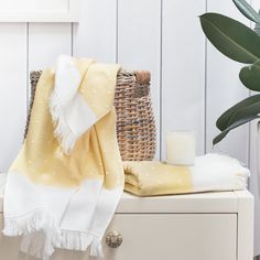 a yellow and white blanket sitting on top of a wooden table next to a wicker basket