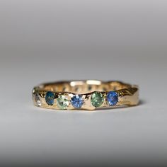 a yellow gold band with blue and green stones on the inside, set against a gray background