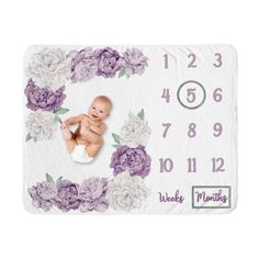 a baby is laying down in front of a clock with purple flowers on the cover