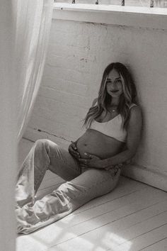 a pregnant woman sitting on the floor next to a window