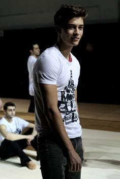 a young man standing on top of a wooden floor next to other men in white shirts