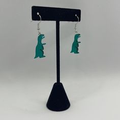 Add a touch of fun to your accessory collection with these charming green dinosaur earrings! Shaped like miniature T-Rex figures, these acrylic earrings are lightweight and perfect for dinosaur enthusiasts of all ages. Featuring a classic fishhook design, they dangle comfortably for a unique and playful style. These earrings make a great gift for anyone who loves quirky, statement jewelry.

Clear Green Dinosaur Earrings 
Dangle Drop Pierced
Acrylic
Silver Plated Earring
Unisex
See Pictures for Measurements Dinosaur Fashion, Dinosaur Earrings, Pink Dinosaur, Green Dinosaur, Pick 3, Playful Style, Acrylic Earrings, Fun Earrings, Earrings Dangle