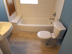 a white toilet sitting next to a bath tub in a bathroom under a window above a sink