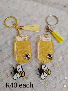 two honey jar key chains with yellow tassels on them, one has a bee and the other has a tassel