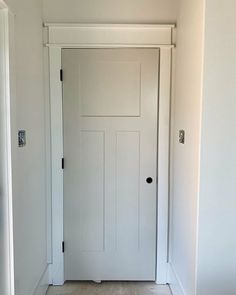 an empty room with a white door and tile floor in front of the door is a light fixture