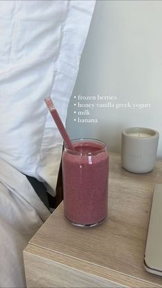 a pink smoothie in a glass next to a laptop on a nightstand with a white pillow