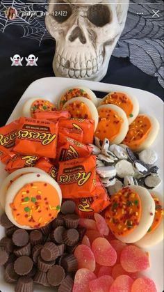 halloween treats are arranged on a plate with a skull in the background and an orange candy bar next to it